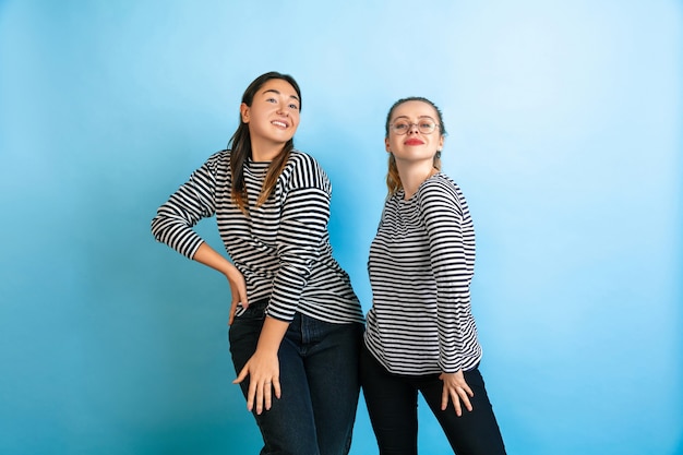 Danser ensemble. Jeunes femmes émotionnelles isolées sur fond de studio bleu dégradé. Concept d'émotions humaines, d'expression faciale, d'amitié, d'annonce. Beaux modèles féminins caucasiens dans des vêtements décontractés.