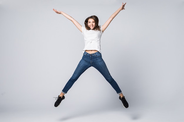 Danseuse aux cheveux longs bruns et heureuse expression faciale souriante sautant en studio isolé sur blanc