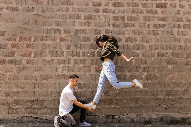 Photo gratuite danseuse sautant sur la main de l'homme contre le mur de pierre