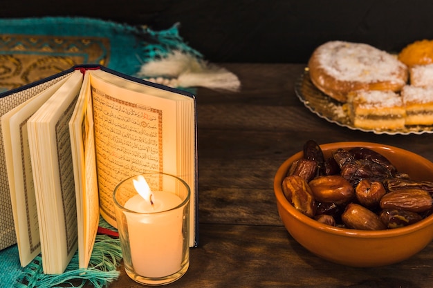 Dates et pâtisserie près de bougie allumée et livre ouvert