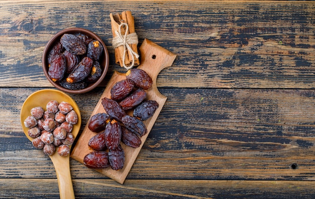 Dattes fraîches dans un bol et une planche à découper avec des noix dans une cuillère en bois et des bâtons de cannelle vue de dessus sur fond de bois