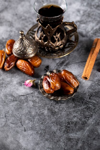 Dattes orientales dans une soucoupe de style ethnique avec un verre de thé et des bâtons de cannelle