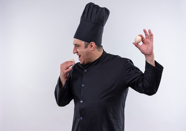 Debout en vue de profil homme d'âge moyen cuisinier en uniforme de chef tenant des oeufs