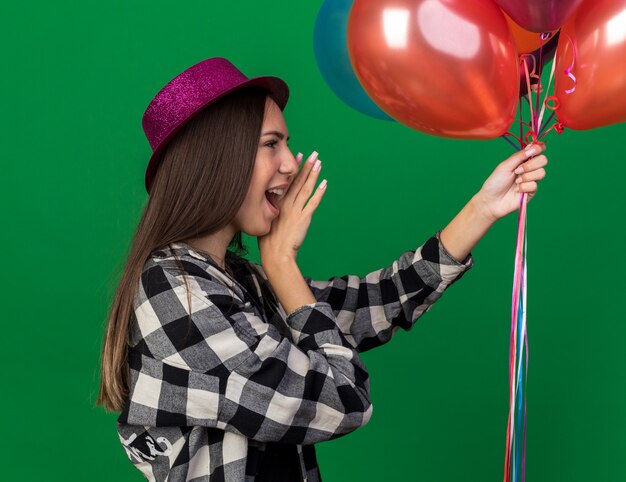 Debout en vue de profil jeune belle fille portant un chapeau de fête tenant des ballons