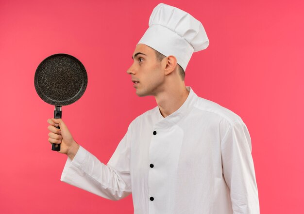 Debout en vue de profil jeune homme cuisinier portant l'uniforme de chef holding poêle à frire