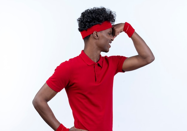 Debout en vue de profil tendu jeune homme sportif afro-américain portant bandeau et bracelet faisant un geste fort sur blanc