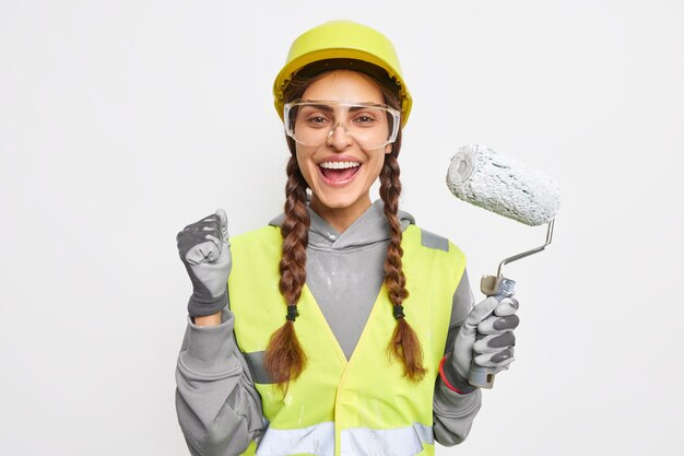 Une décoratrice positive serre le poing de joie tient un rouleau de peinture prêt pour la rénovation de la chambre