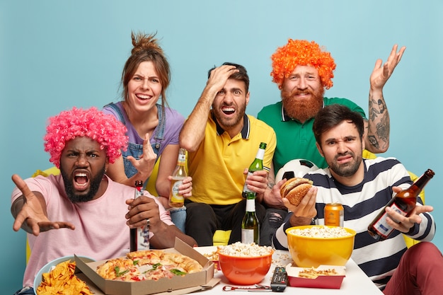 Déçus, quatre hommes et une femme regardent un match de sport, insatisfaits de l'échec de l'équipe, boivent de la bière, prennent une collation, expriment une réaction négative, de mauvaises émotions, posent ensemble sur un canapé à la maison. L'équipe perd.