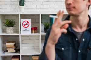 Photo gratuite défocalisation homme avec une cigarette devant une affiche non fumeur sur une étagère