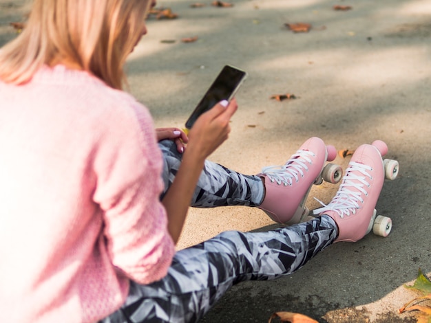 Défocalisé haute angle de femme en patins à roulettes à la recherche de smartphone