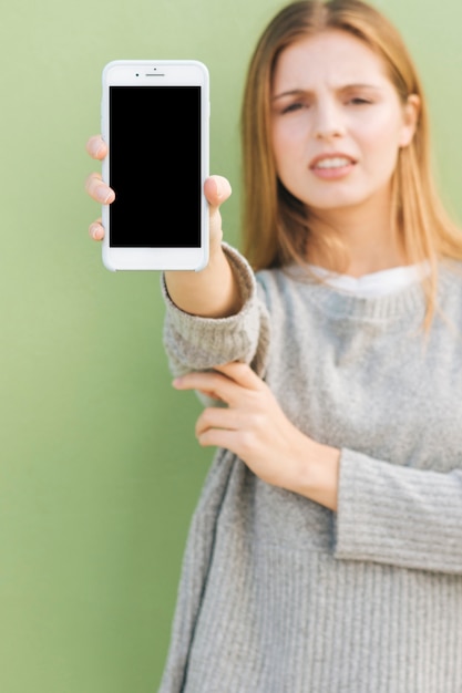 Défocalisé jeune femme montrant l&#39;écran du téléphone mobile vers la caméra