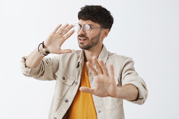 Dégoûté élégant barbu posant contre le mur blanc