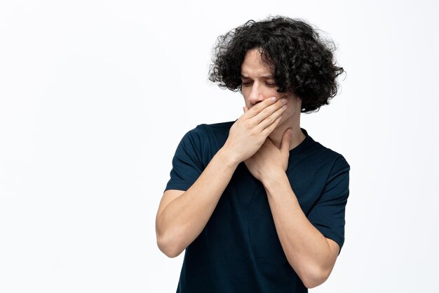 Dégoûté jeune bel homme regardant vers le bas en gardant la main sur la gorge en fermant la bouche avec la main ayant mal à la gorge isolé sur fond blanc