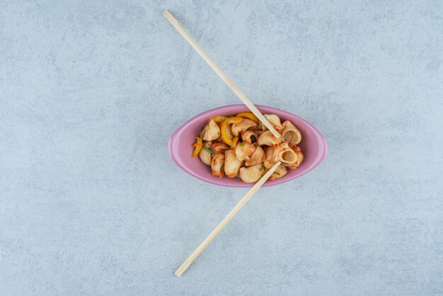 Délicieuse assiette rose avec macaroni et baguettes sur fond sombre. Photo de haute qualité