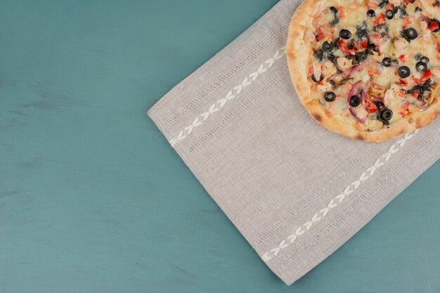 Délicieuse pizza chaude aux olives et tomates sur une surface bleue.