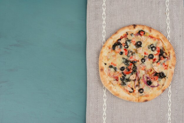 Délicieuse pizza chaude aux olives et tomates sur une surface bleue.