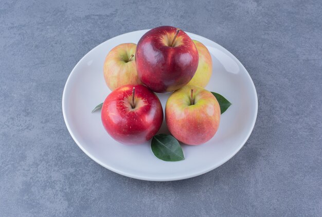 Délicieuse pomme avec des feuilles sur plaque sur table en marbre.