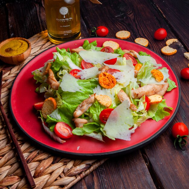 Délicieuse salade dans une assiette rouge avec de l'huile high angle view sur un fond en bois