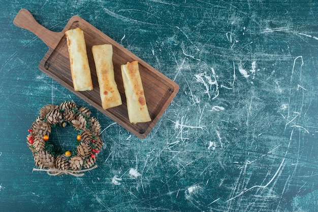 De délicieuses crêpes sur un petit plateau à côté d'une couronne de pomme de pin sur bleu.