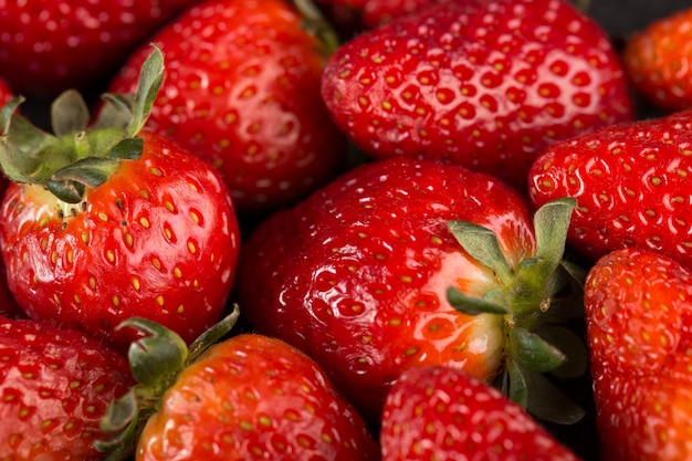 Délicieuses fraises rouges mûres avec des feuilles vertes sur un bureau sombre