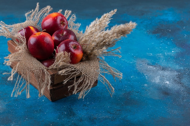 Délicieuses pommes rouges brillantes placées dans une boîte en bois.