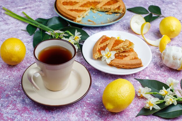 Délicieuses tranches de tarte au citron avec des citrons frais et une tasse de thé, vue du dessus