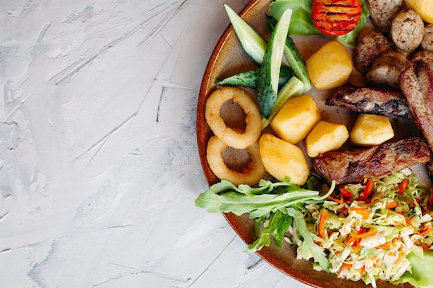 Délicieux apéritifs de restaurant pour la bière salade de légumes pommes de terre bouillies cuisses de poulet grillées saucisses à l'oignon rôti concombres tomates et sauces ketchup et mayo posés sur une plaque d'argile