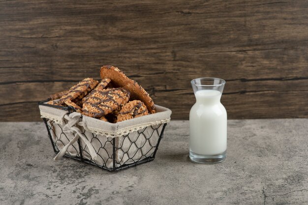 Délicieux biscuits multigrains frais avec glaçage au chocolat dans un panier avec un bocal en verre de lait.