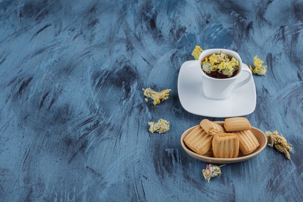 Délicieux biscuits avec tasse de tisane sur une surface bleue.