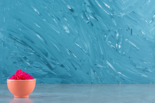 Un délicieux chou rouge fermenté se trouve dans un bol, sur la table bleue.