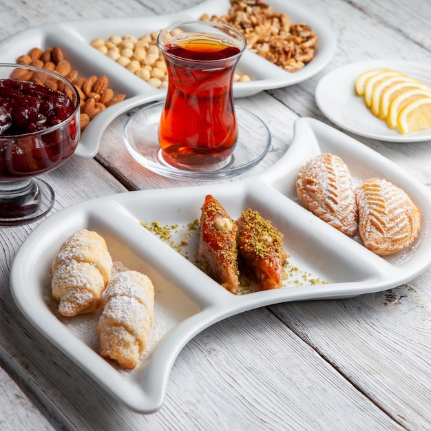 De délicieux desserts avec du thé, des noix, de la confiture de fruits, du citron en tranches sur un fond en bois blanc, vue en plongée.