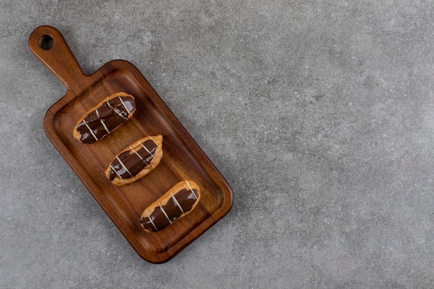 De délicieux éclairs au chocolat sur une plaque en bois sur une surface grise