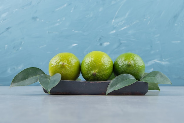 De délicieux fruits de citron vert avec des feuilles sur une plaque noire.