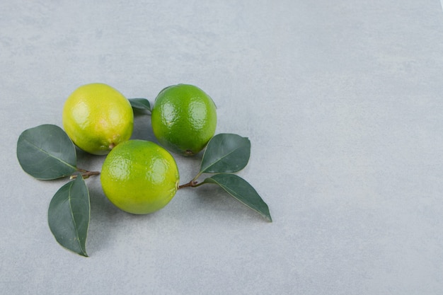 De délicieux fruits de citron vert avec des feuilles sur une table en pierre.