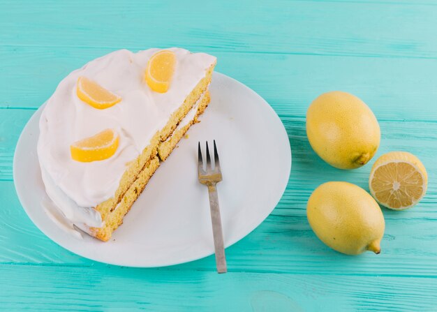 Photo gratuite délicieux gâteau au citron dans l'assiette avec une fourchette et citrons sur une table en bois