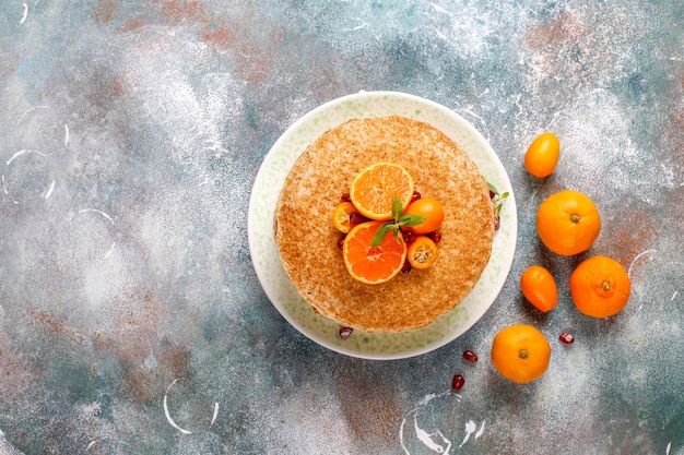 Photo gratuite délicieux gâteau aux crêpes maison décoré de graines de grenade et de mandarines.