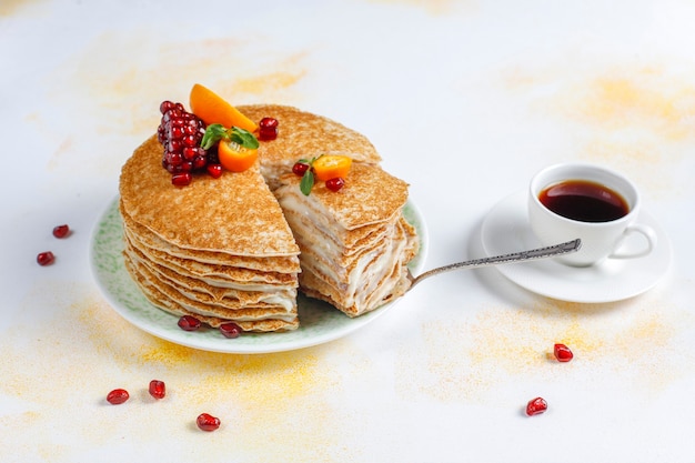 Délicieux gâteau de crêpes maison décoré de graines de grenade et de mandarines.