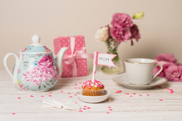 Délicieux gâteau avec drapeau décoratif avec titre de maman près de théière, fleurs et coupe