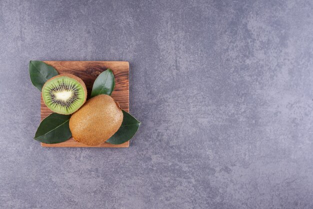 Délicieux kiwi tranché avec des feuilles placées sur une assiette en bois.