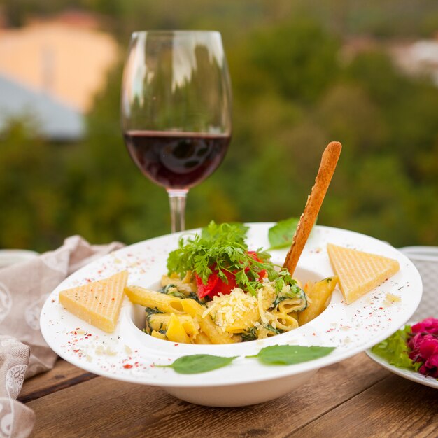 Délicieux macaroni mélangé à une salade de vin et de fromage dans une assiette avec village en arrière-plan, vue latérale.