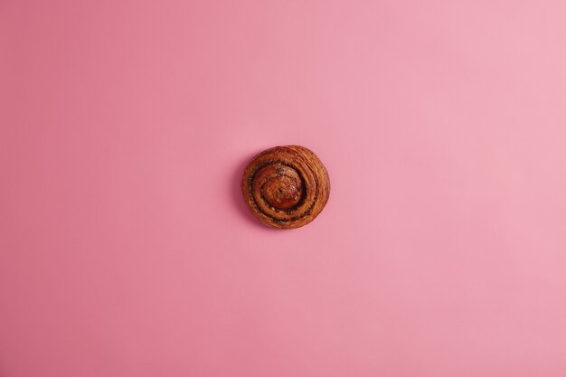 Délicieux pain à la cannelle appétissant fait maison avec du sucre caramélisé et garniture de confiture isolé sur fond rose. Rouleau de tourbillon savoureux prêt à manger. Boulangerie, nutrition, concept d'aliments malsains.