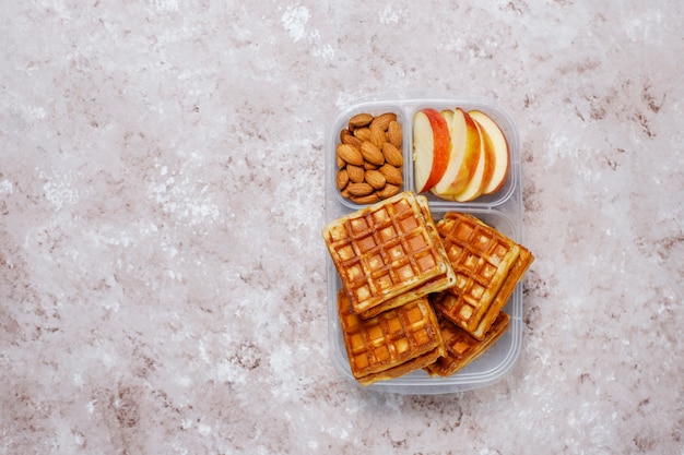 Délicieux petit déjeuner avec amandes, tranches de pommes rouges, gaufres, croissants sur boîte à lunch en plastique à la lumière