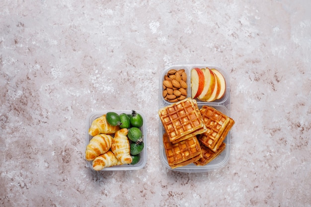 Délicieux petit déjeuner avec amandes, tranches de pommes rouges, gaufres, croissants sur boîte à lunch en plastique à la lumière