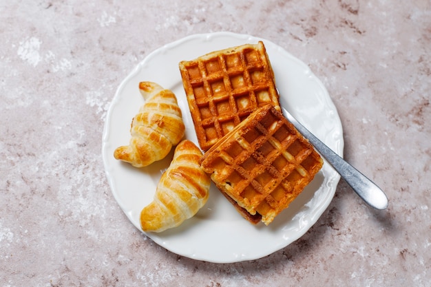 Délicieux petit déjeuner avec café, jus d'orange, gaufres, croissants, confiture, pâte de noix à la lumière, vue de dessus