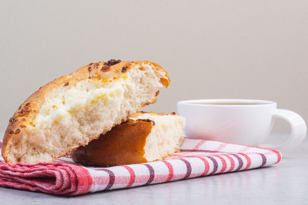 Délicieux petit pain tranché sur une serviette à côté d'une tasse de thé, sur le marbre.