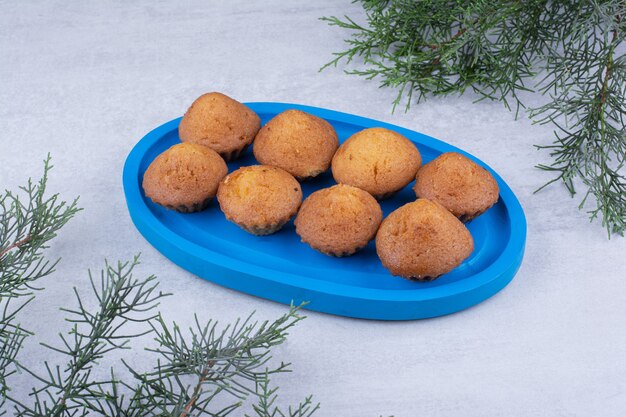 Délicieux petits gâteaux sur plaque bleue avec branche de pin.