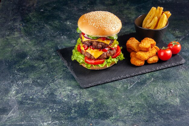 Délicieux sandwich sur plateau de couleur sombre et pépites de poulet tomates frites sur le côté gauche sur une surface noire