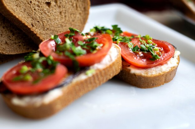 De délicieux sandwichs aux toasts bruns avec des légumes frais tels que des tomates rouges en tranches et des aubergines frites noires avec des verts sur le dessus sur une plaque blanche