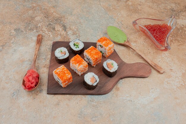Délicieux sushis au caviar, gingembre et vasabi sur plaque en bois.