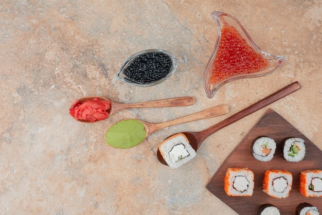 Délicieux sushis au caviar, gingembre et vasabi sur plaque en bois.